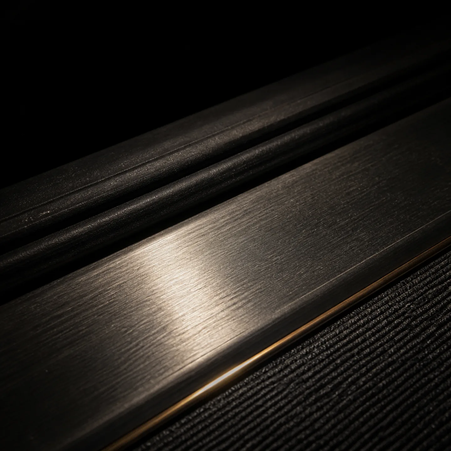 A brushed metal sill plate beneath ribbed black door trim, edged with a thin brass line.
