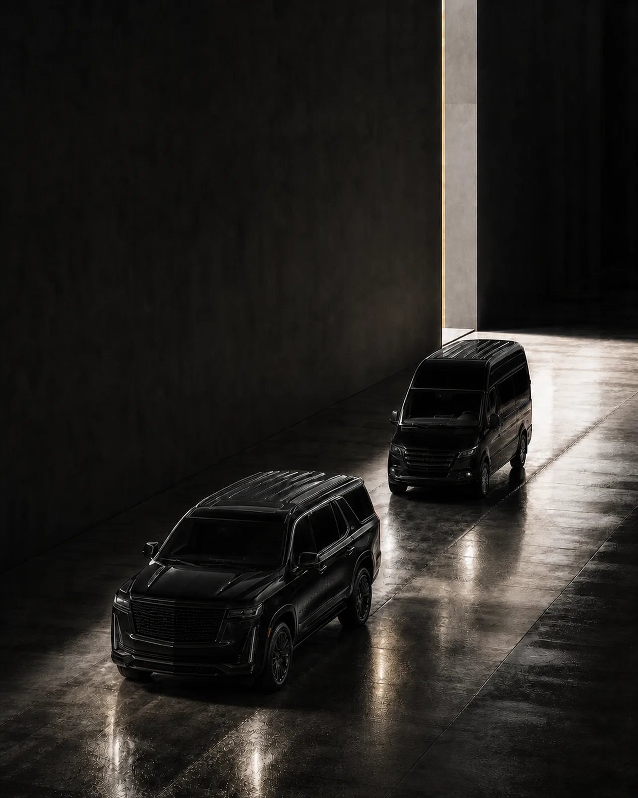 An overhead view of a black Cadillac Escalade followed by a black Mercedes-Benz Sprinter van driving toward a bright doorway in a dark space.
